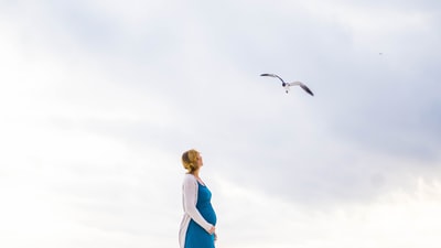 女人在蓝色和白色礼服站在那儿看着飞走的小鸟
